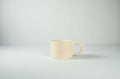 Mug in ceramica artigianale Kalakera color beige con finitura opaca e setosa. Un oggetto di design essenziale che celebra la bellezza delle forme organiche e del minimalismo caldo.