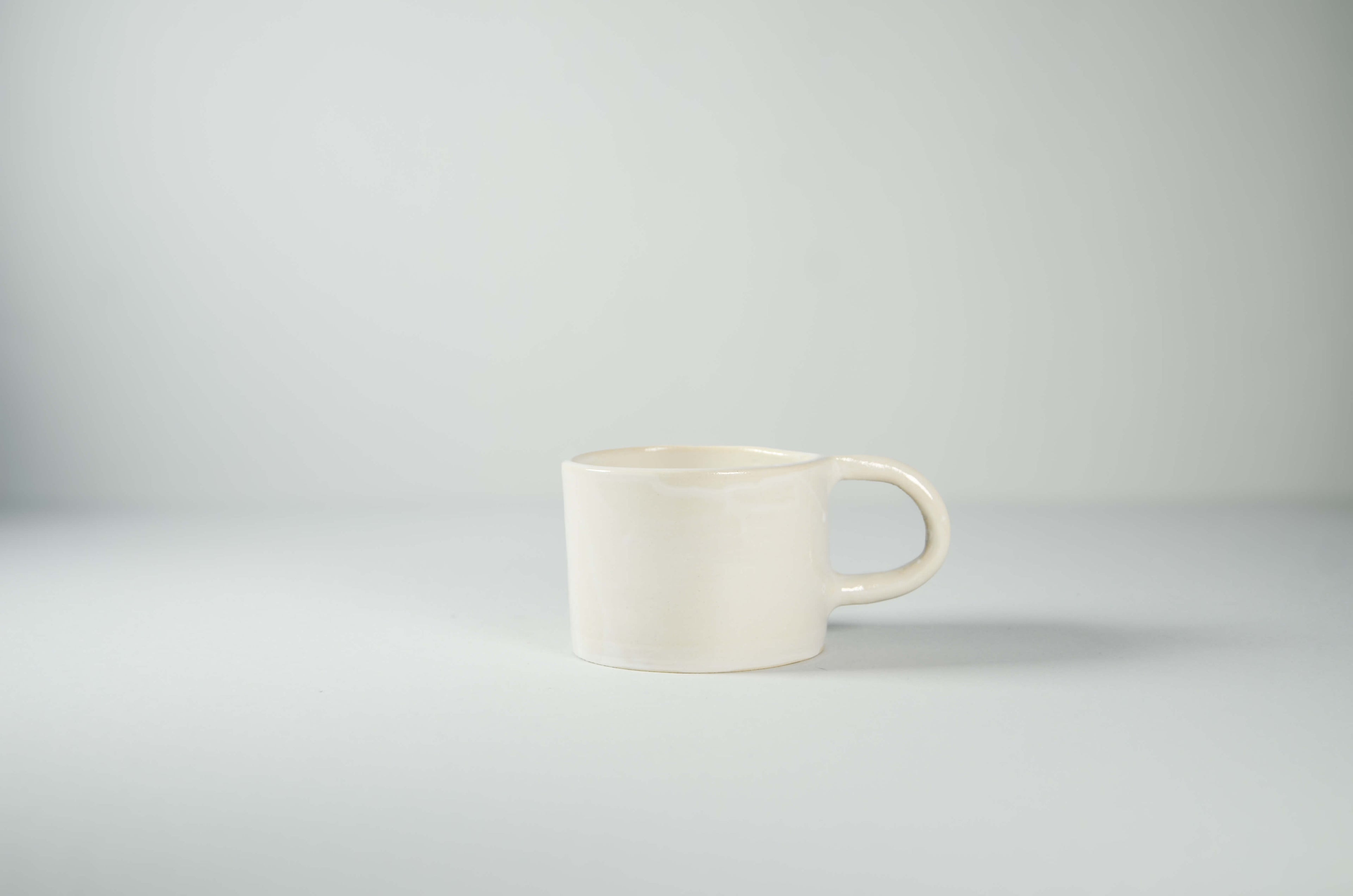 Tazza in ceramica artigianale Kalakera color bianco con finitura lucida. Un pezzo di design minimale dalle linee pulite e forme organiche, ideale per una cucina moderna.