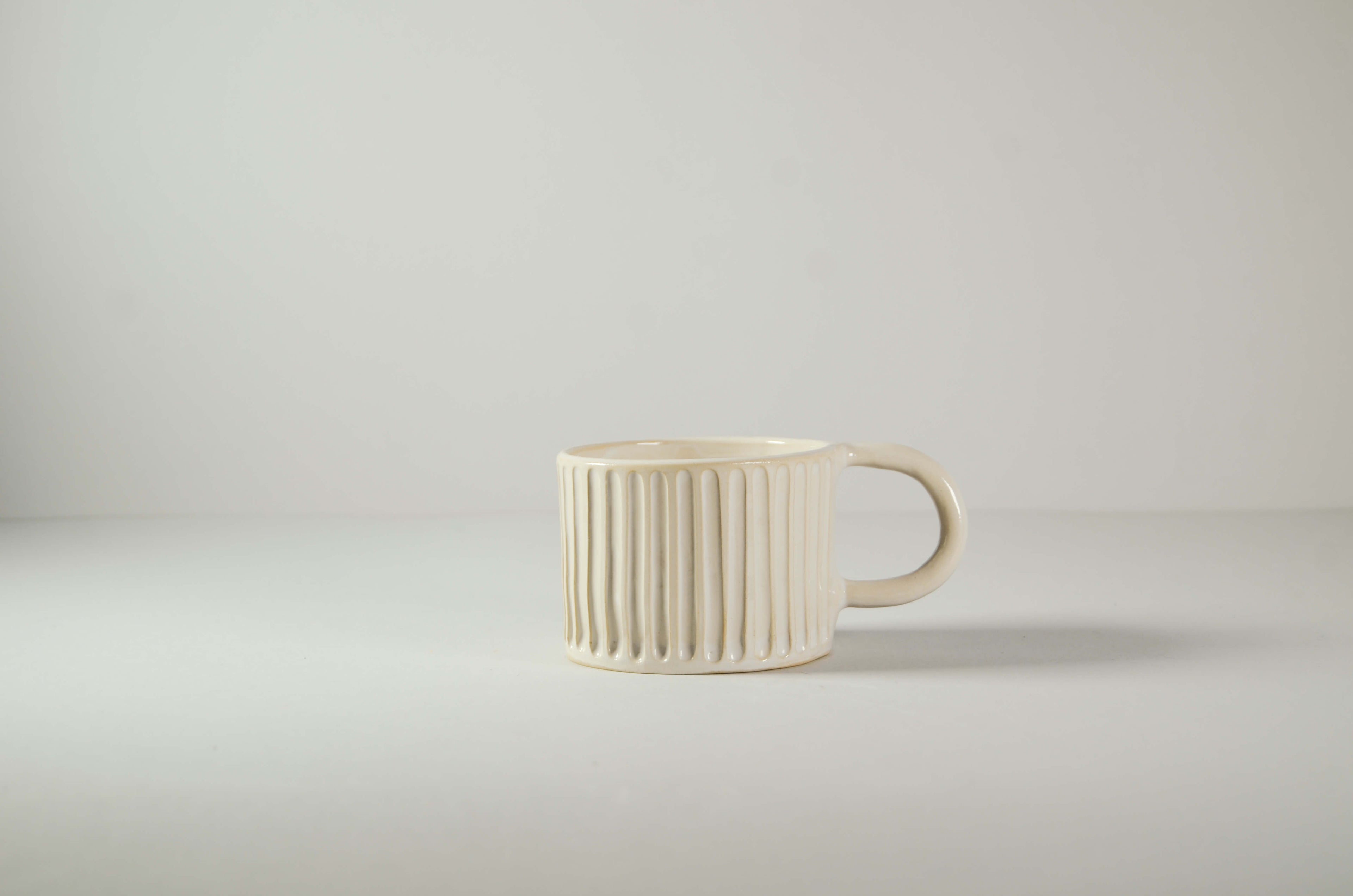 Mug in ceramica artigianale Kalakera color bianca con lavorazione canneté a coste verticali. Un pezzo dal design materico e minimalista, ideale per un arredamento in stile Japandi.