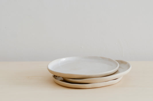 tre piatti piani piccoli fatti a mano in ceramica e di colore beige all'esterno e bianco all'interno