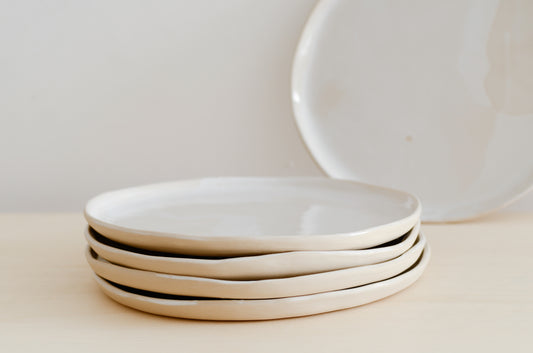 quattro piatti piani in primo piano e uno sullo sfondo, fatti a mano in ceramica e di colore beige all'esterno e bianco all'interno