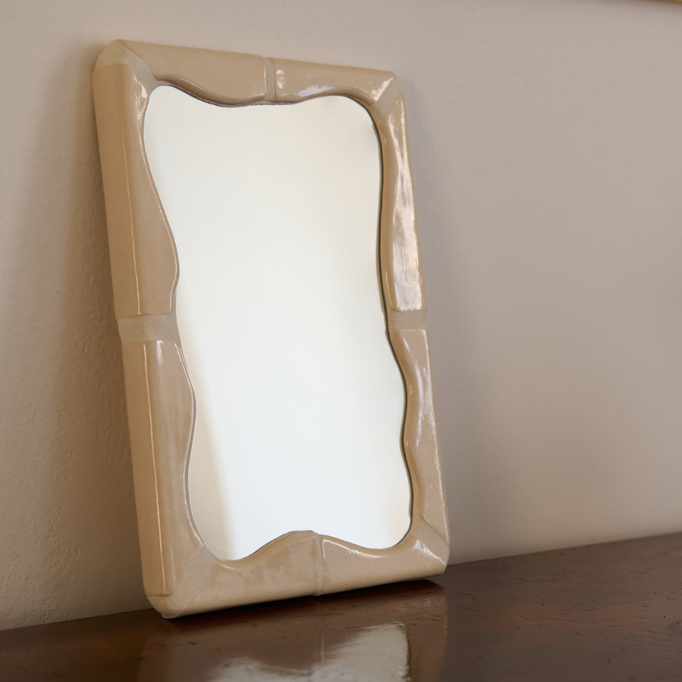 Specchio rettangolare Kalakera con cornice in ceramica artigianale color sabbia. Il design è caratterizzato da un profilo interno a onde fluide e una struttura a moduli, incarnando un'estetica materica e scultorea.