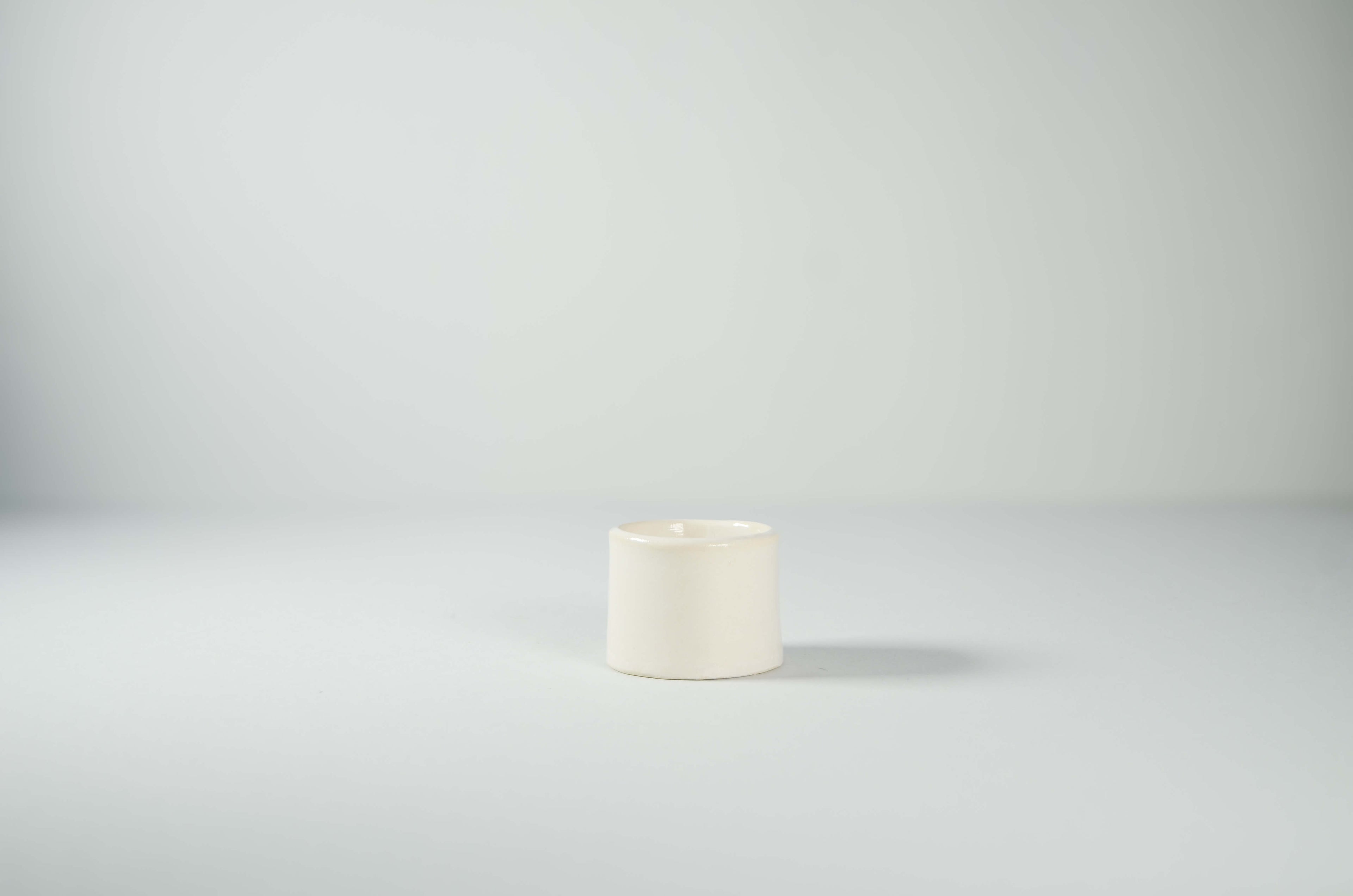 Tazzina da caffè espresso Kalakera in ceramica smaltata bianca liscia. Un design essenziale e scultoreo caratterizzato da linee pulite e volumi minimalisti, tipico dell'artigianato artistico contemporaneo.