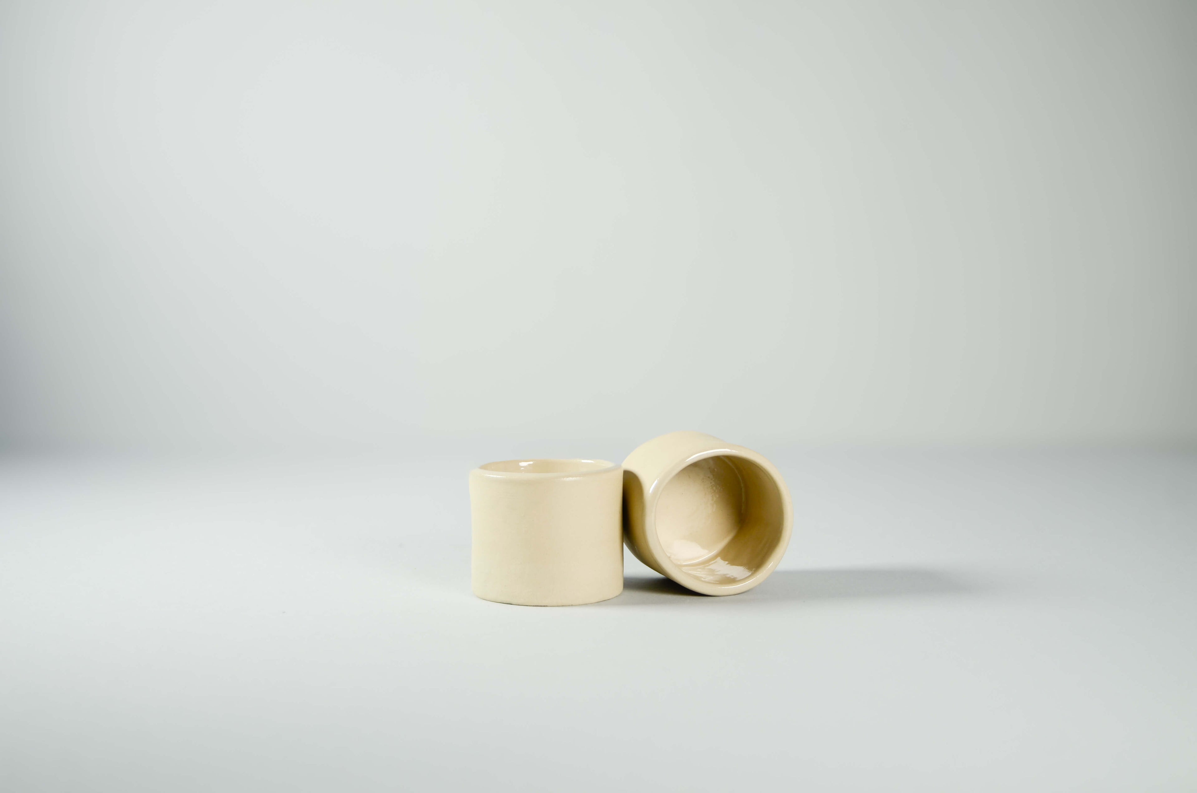 Coppia di tazzine da caffè espresso Kalakera in ceramica liscia color beige. Un design essenziale e scultoreo caratterizzato da linee pulite e volumi minimalisti, tipico dell'artigianato artistico contemporaneo.