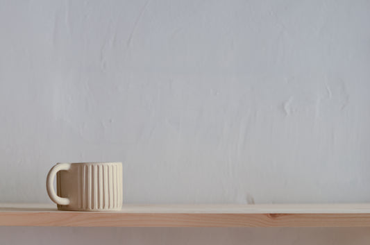 Nella foto appare una tazza è in ceramica fatta a mano, di colore beige, con il manico e con una decorazione a righe fatte con incisione