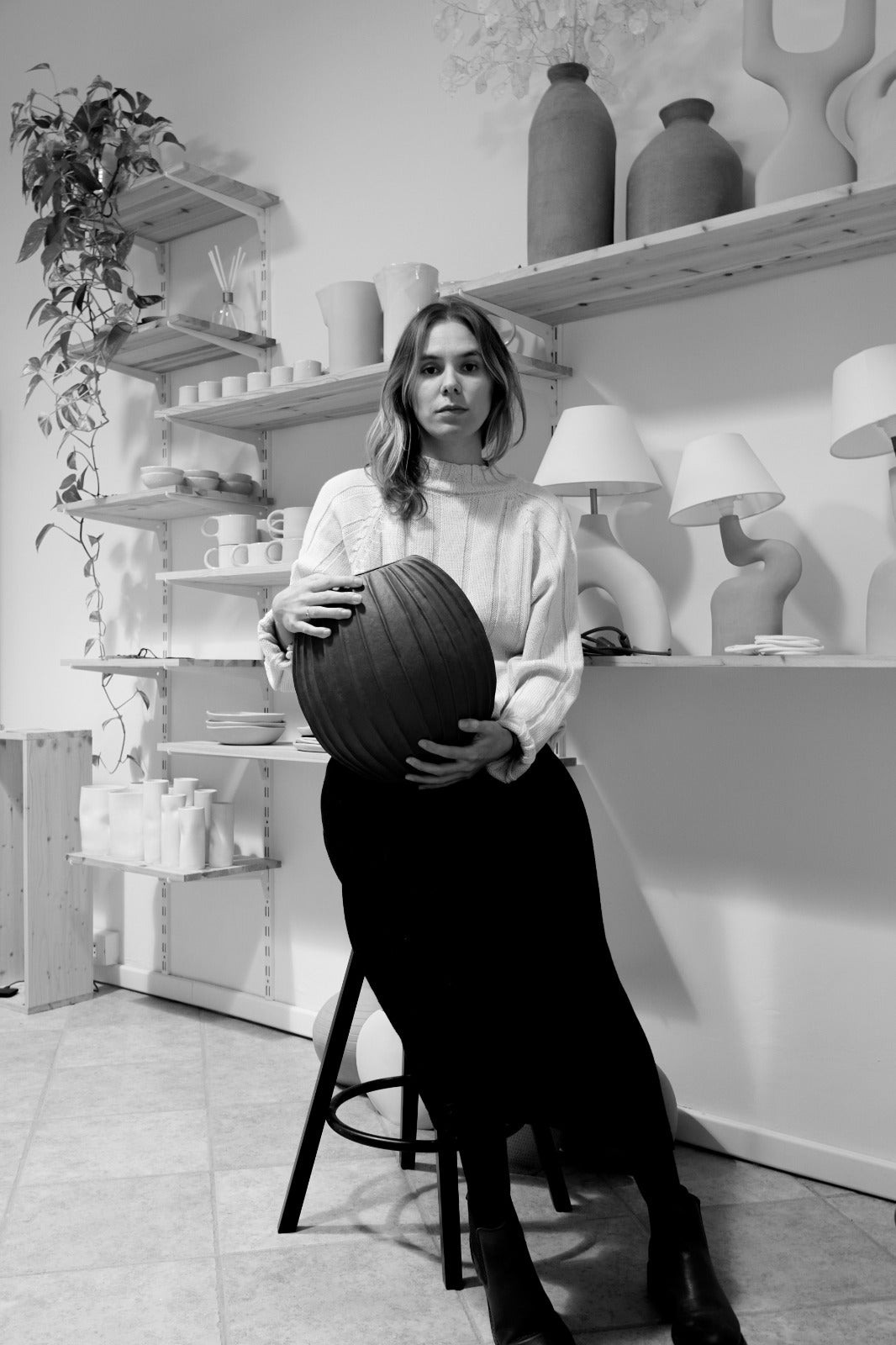 ritratto di giovane donna, tiene in mano un vaso fatto in ceramica. dietro di lei vi sono altri oggetti in ceramica, tra cui tazze, caraffe, lampade e vasi